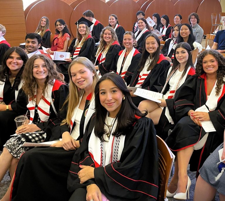 Students in graduation robes with red and white Honors stoles smile for picture.