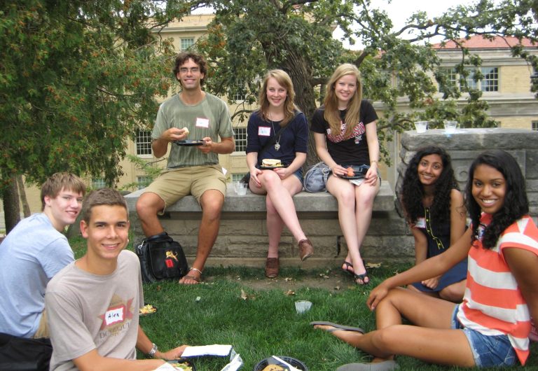 A small group of students with name tags sit outside on Observatory Hill, enjoying food and smiling for the camera.