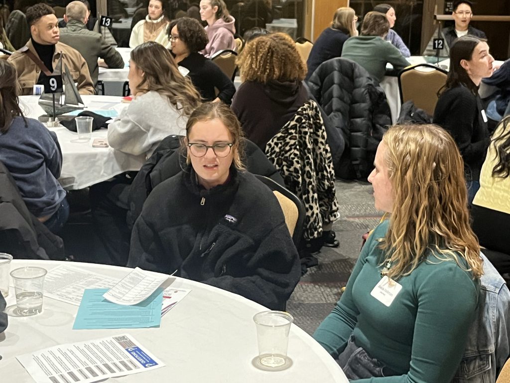 An undergraduate asks a graduate student talking together at a round table