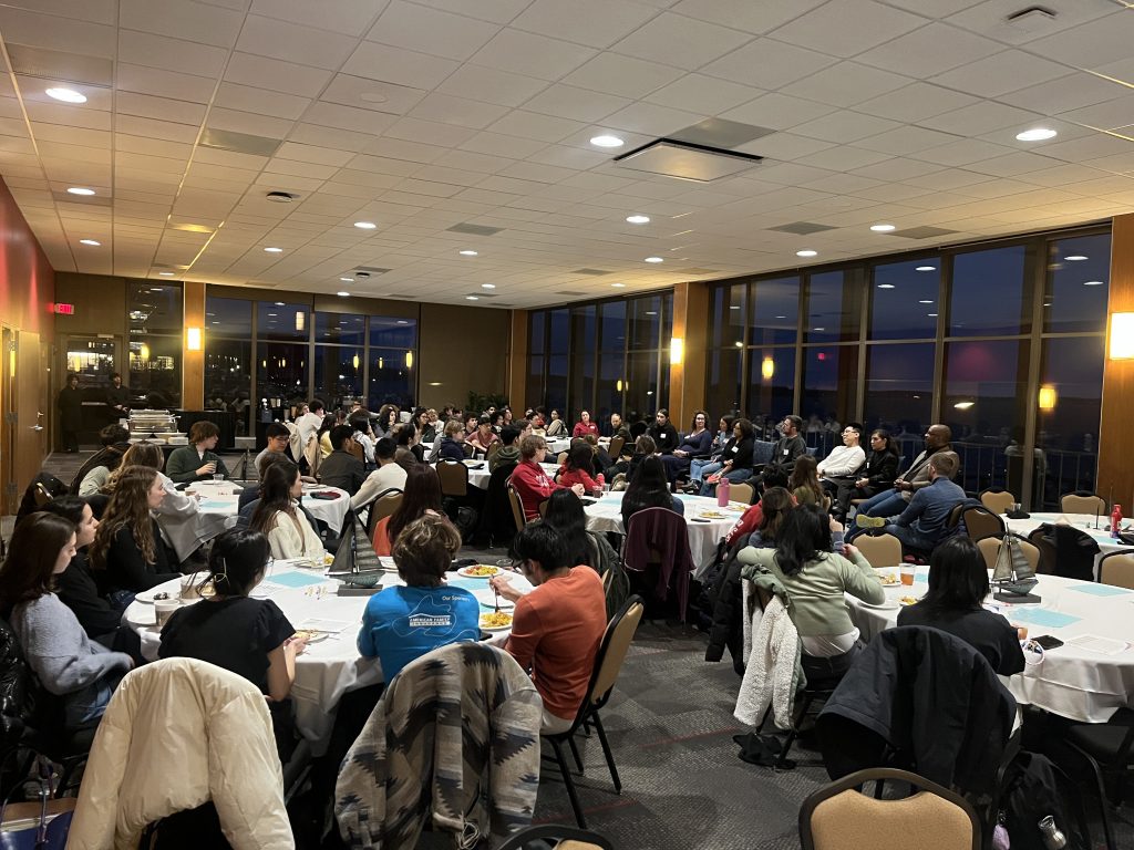 Full room of people with panelists seated at the front