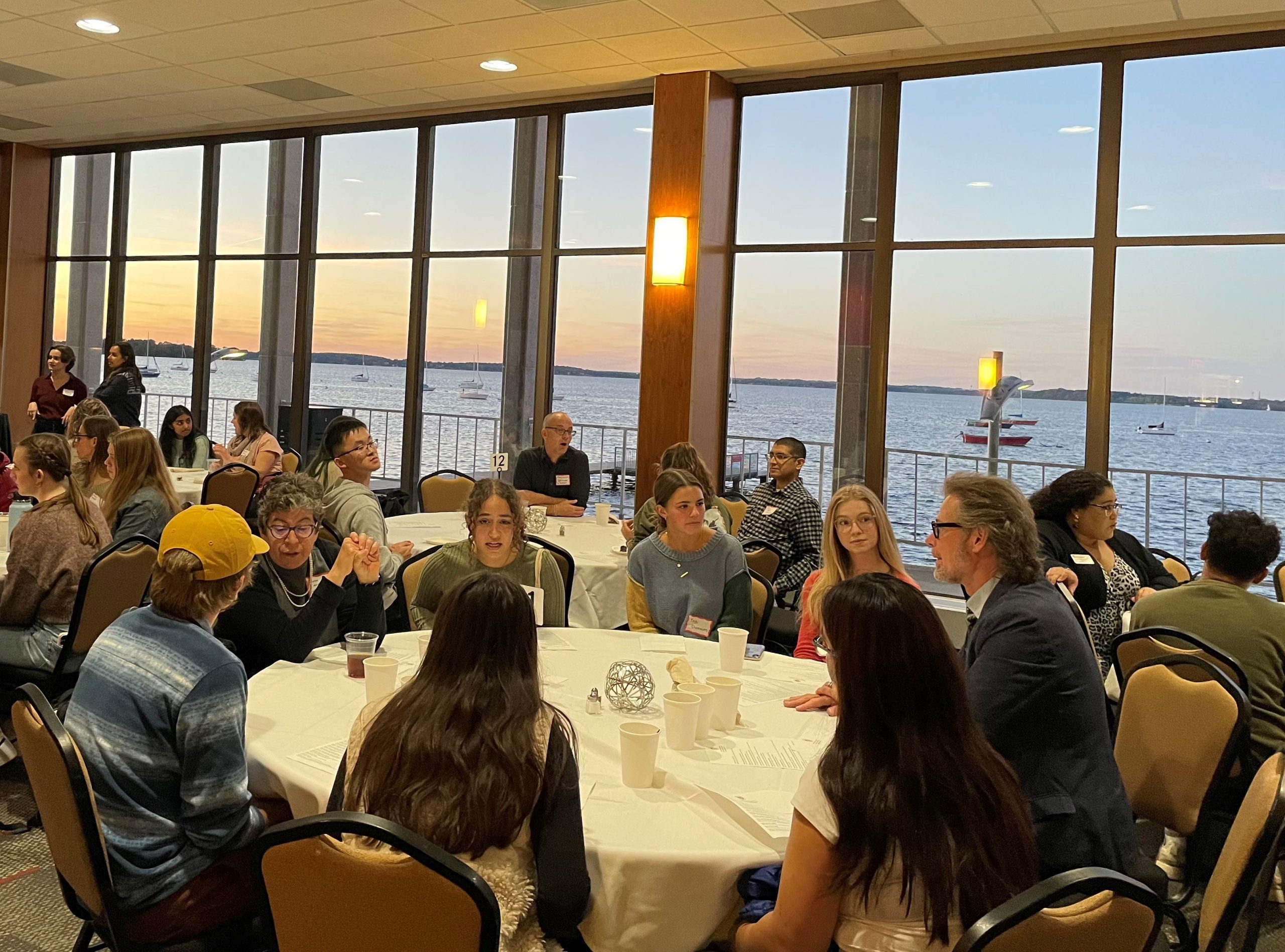 People talking at tables with view of the sunset through the windows