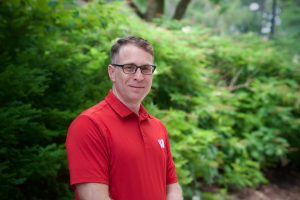 Photo of Dr. Kapust in a red Wisconsin polo in front of some greenery