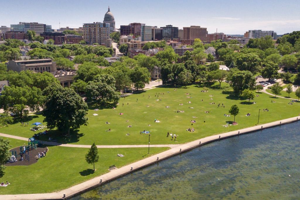 Picture of James Madison Park from Lake Mendota, featuring a green lawn, trees, and the capitol in the background
