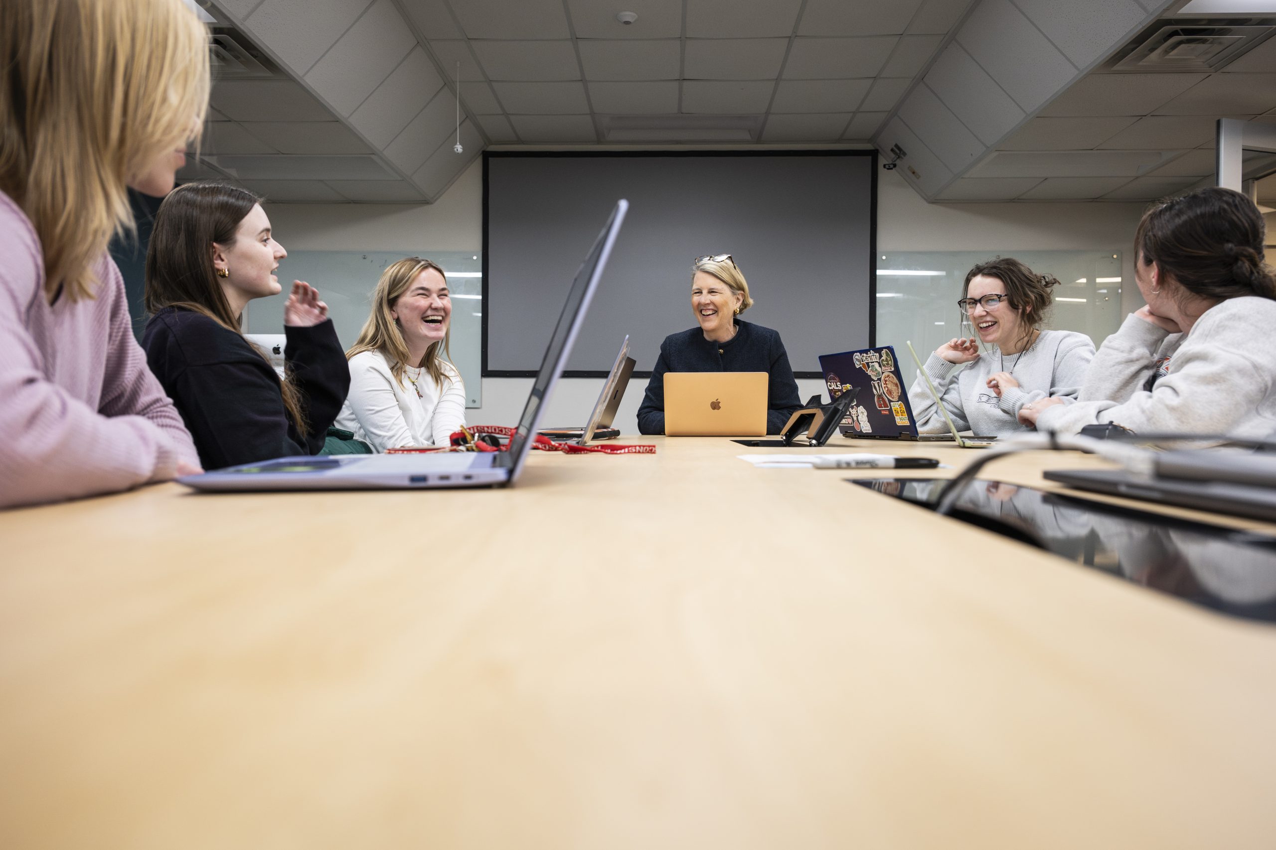 Students gather around a table with a faculty member to discuss a class topic.